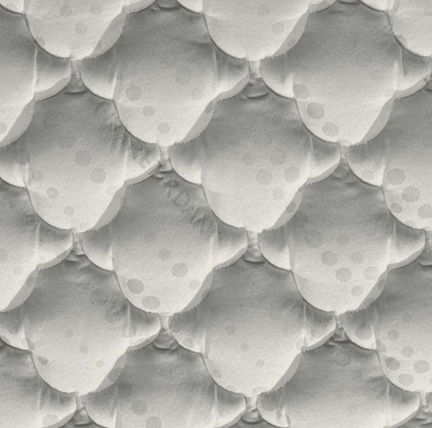 Close-up macro do tecido com tecnologia Fire Retardant. A imagem destaca o padrão de costura matelassê em formato de conchas ou escamas sobrepostas. O tecido é de cor cinza claro com pequenos detalhes pontilhados. A expressão 'FIRE RETARDANT' está discretamente gravada em baixo-relevo nas fibras, sinalizando a propriedade de resistência ao fogo do material.