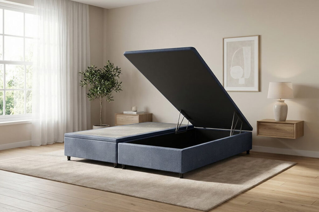 Ambiente de quarto moderno com a base Box Baú da Cama Elegance em azul escuro. O móvel está com o compartimento de armazenamento aberto, posicionado sobre um tapete bege em um quarto iluminado.